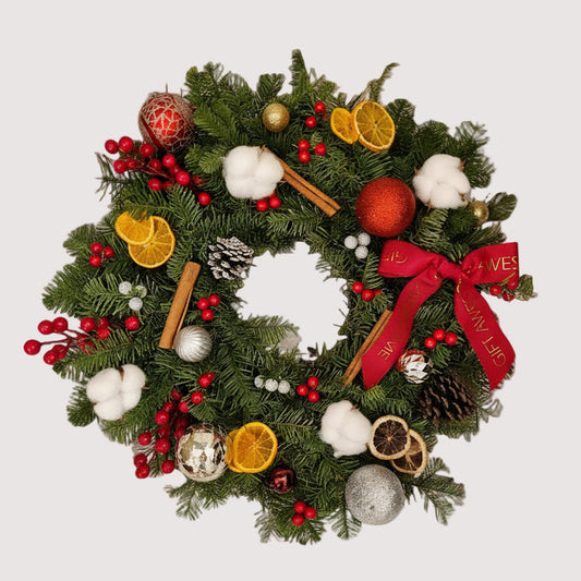 A Christmas wreath decorated with a variety of dried fruits, pine cones, cotton flowers, and Christmas decorations, with a red bow and fresh noble fir.